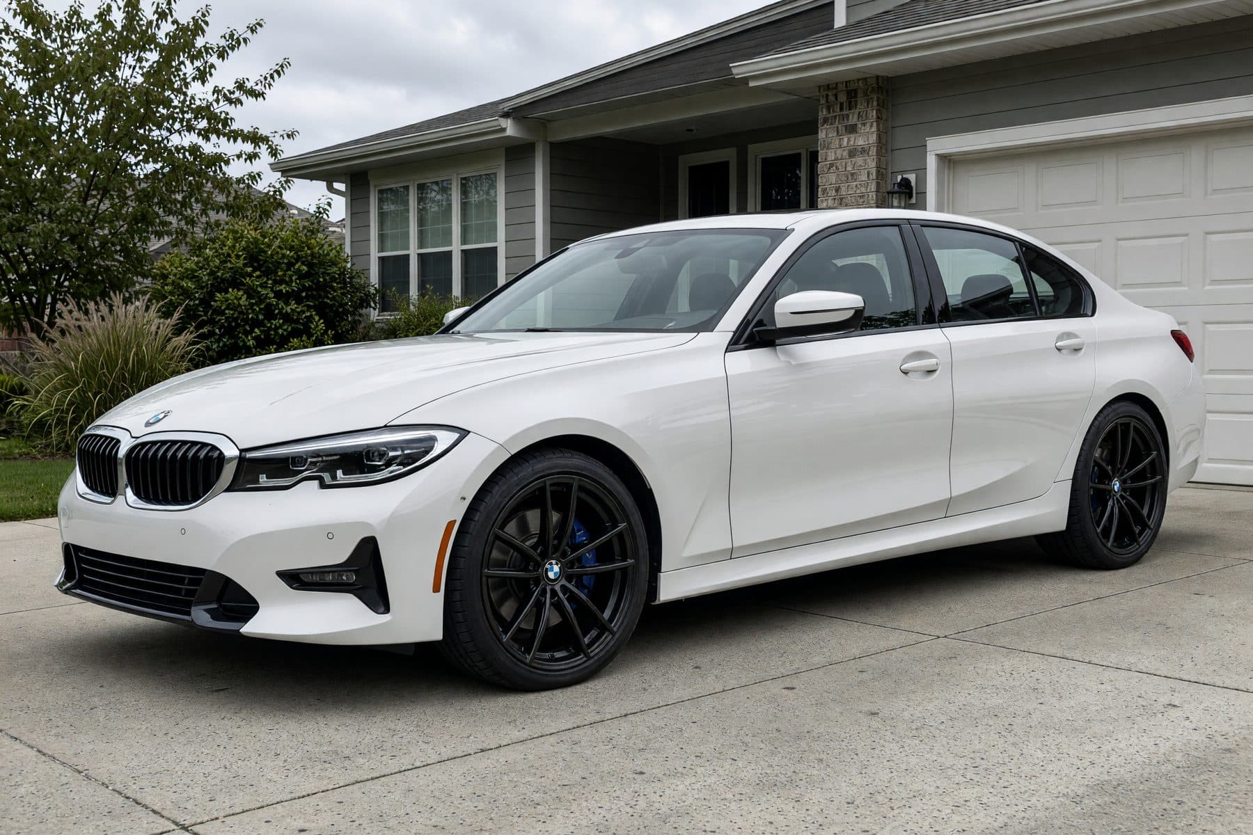 The same white BMW 3 Series in the same driveway, wearing the Aero-5 Flow-Formed wheel (19" · gloss black · flow-formed).