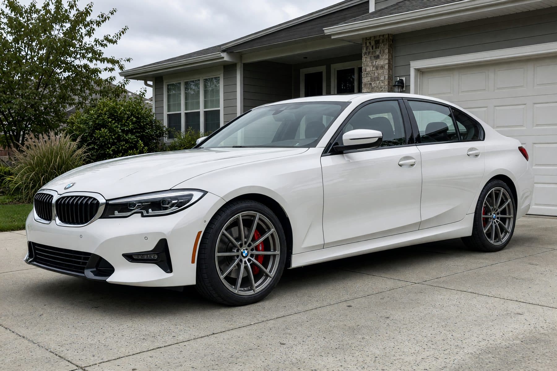 The same white BMW 3 Series in the same driveway, wearing the TrackSpec TS-10 wheel (20" · matte gunmetal · ten-spoke).