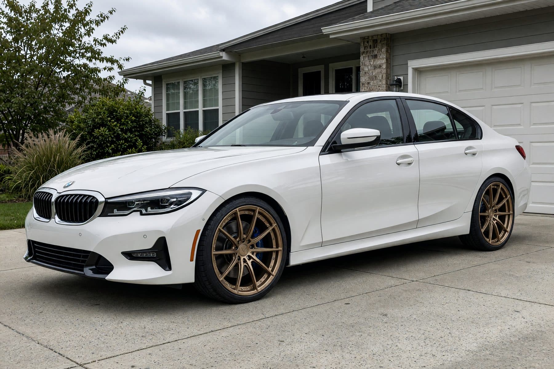 The same white BMW 3 Series in the same driveway, wearing the Vortex R Forged wheel (20" · satin bronze · forged monoblock).